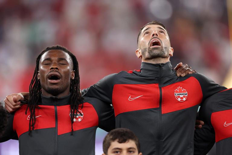 DOHA, QATAR - DECEMBER 01: Sam Adekugbe and Steven Vitoria of Canada sign the national anthem prior to the FIFA World Cup Qatar 2022 Group F match between Canada and Morocco at Al Thumama Stadium on December 01, 2022 in Doha, Qatar. (Photo by Richard Heathcote/Getty Images)